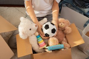 Teenager sorting and collect kid toys, clothes into boxes at home. Donations for charity, help low income families, declutter home, sell online, moving into new home, recycling, sustainable living
